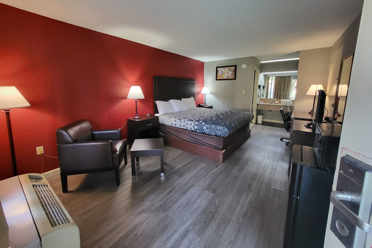 A hotel room with a bed, a desk, a chair, a desk lamp, a heater, and a TV.