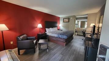Ein Hotelzimmer mit Bett, Schreibtisch, Stuhl, Schreibtischlampe, Heizung und Fernseher.