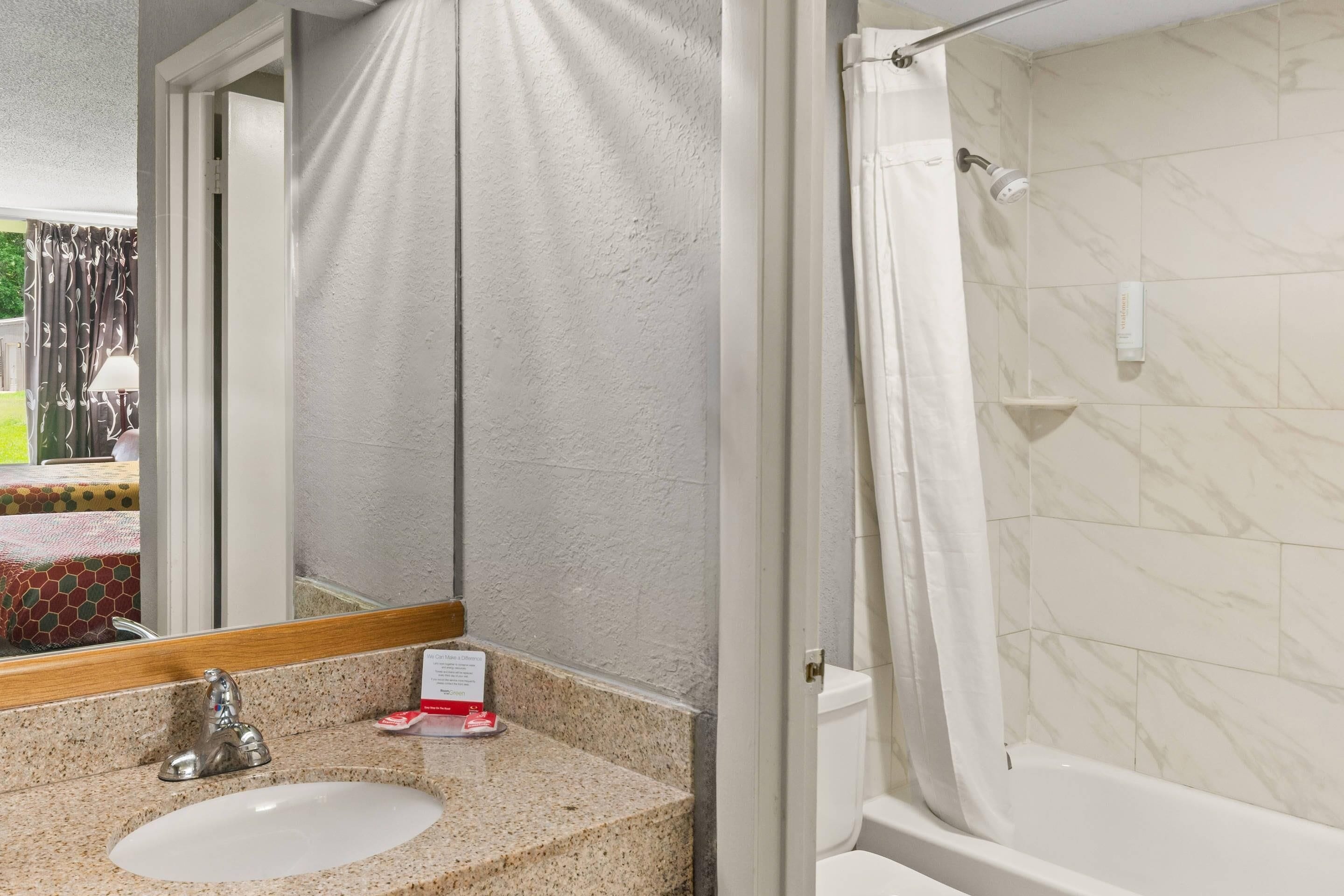A bathroom with a marble-tiled shower, a sink with a mirror, and a towel rack.