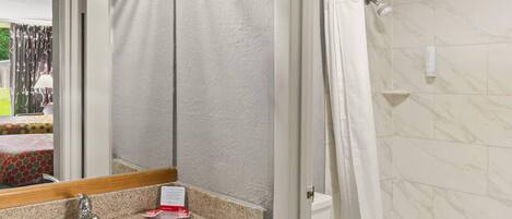 A bathroom with a marble-tiled shower, a sink with a mirror, and a towel rack.
