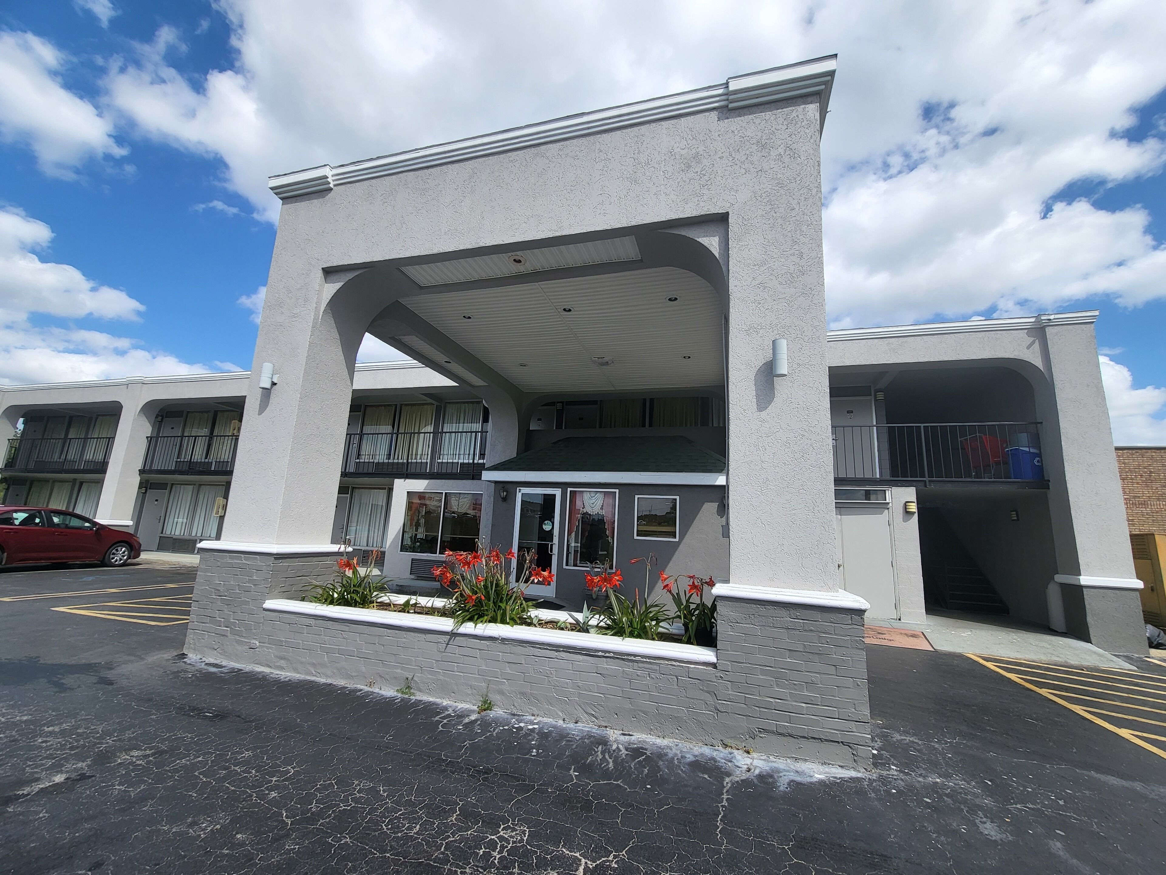 A building with a covered entrance, a parking lot, and a red car parked in the lot.