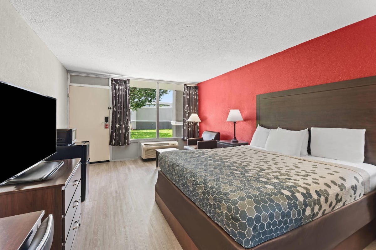 A hotel room with a bed, a desk, a TV, and a window with curtains.