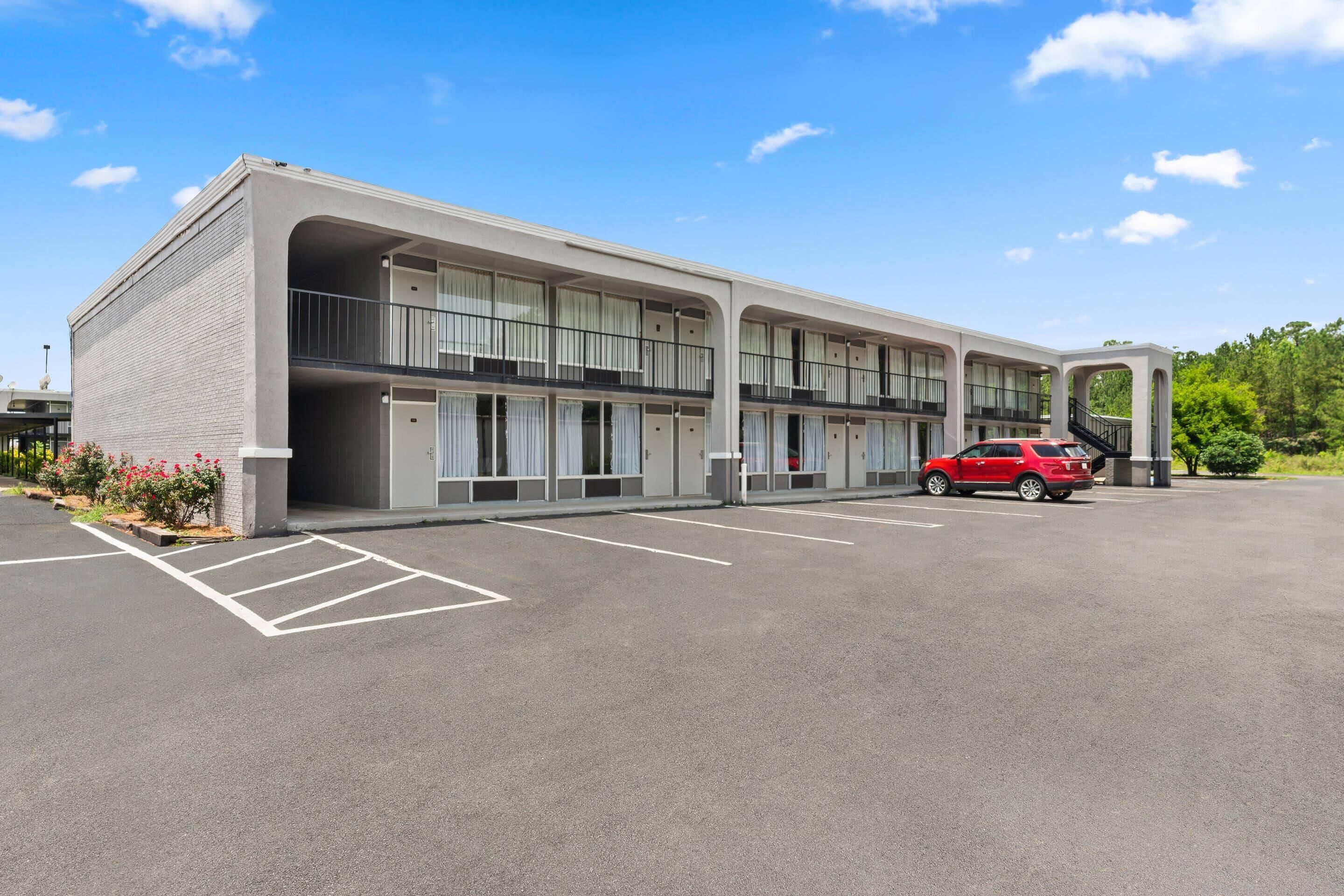 A modern building with a parking lot and a red car.