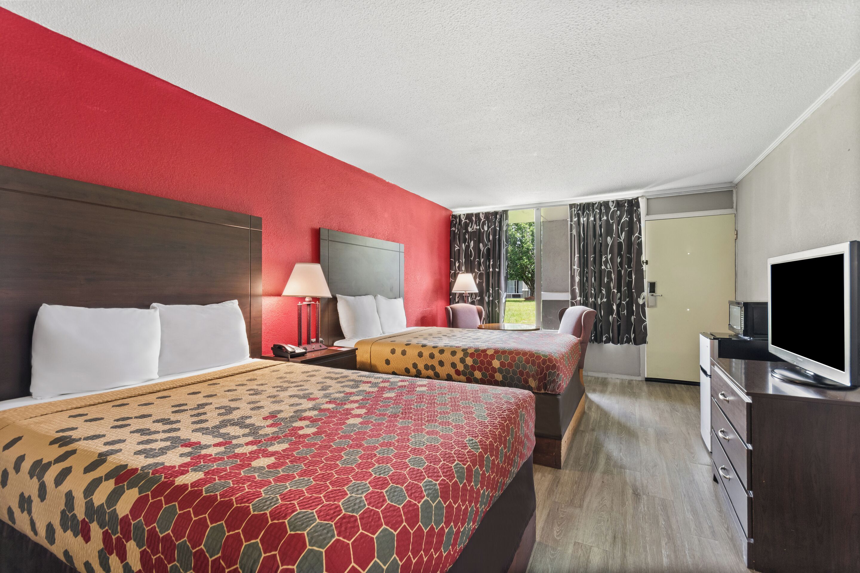 A hotel room with two beds, a TV, a desk, and a window with curtains.