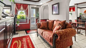 A cozy living area with a red sofa, a coffee machine, and a dining table with chairs. - Econo Lodge Andalusia (Andalusia)