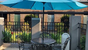 A patio with a table and chairs under a blue umbrella, surrounded by a brick wall and metal fencing. - Econo Lodge Andalusia (Andalusia)