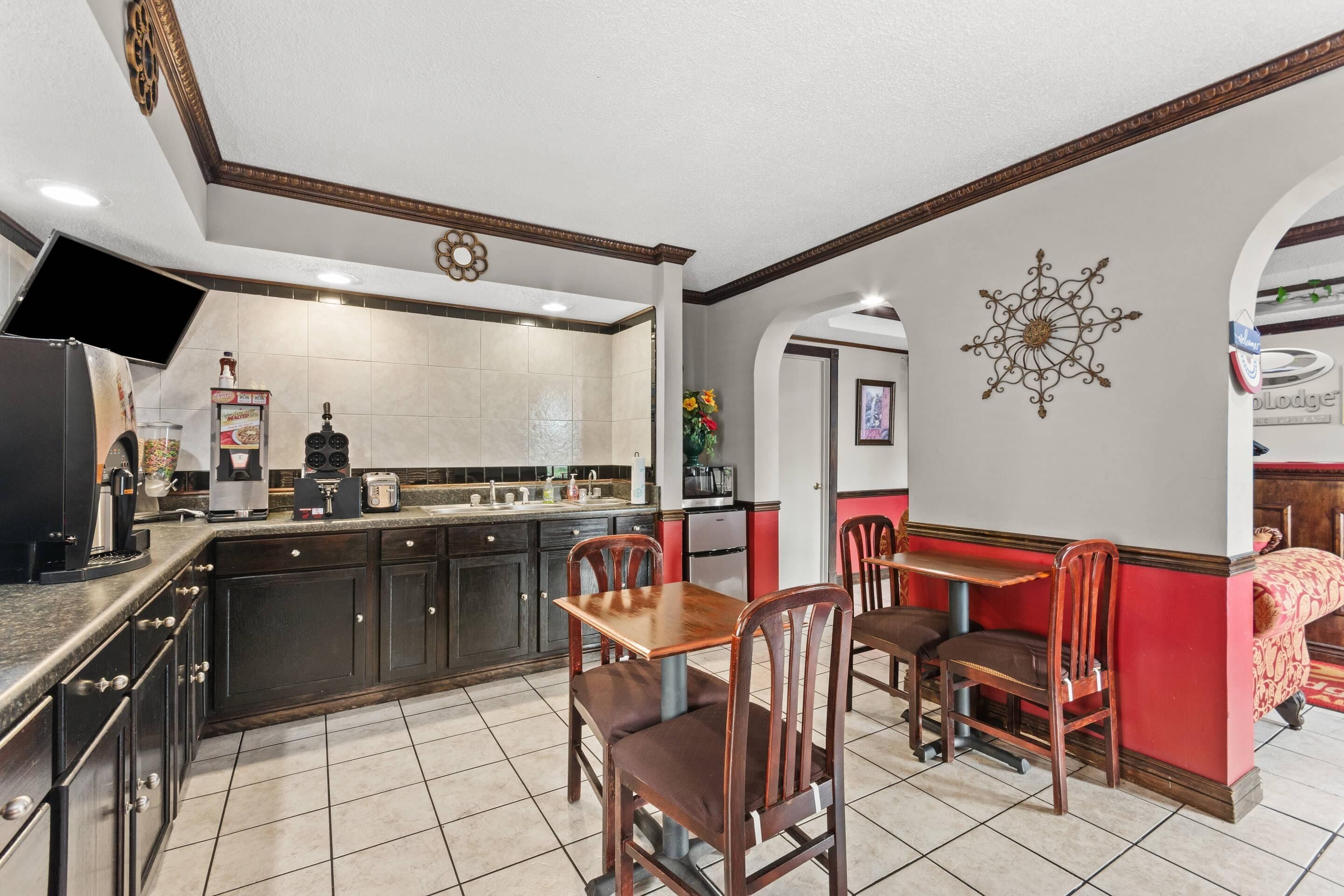 A kitchen with dark wooden cabinets, a dining table with chairs, and a red accent wall.
