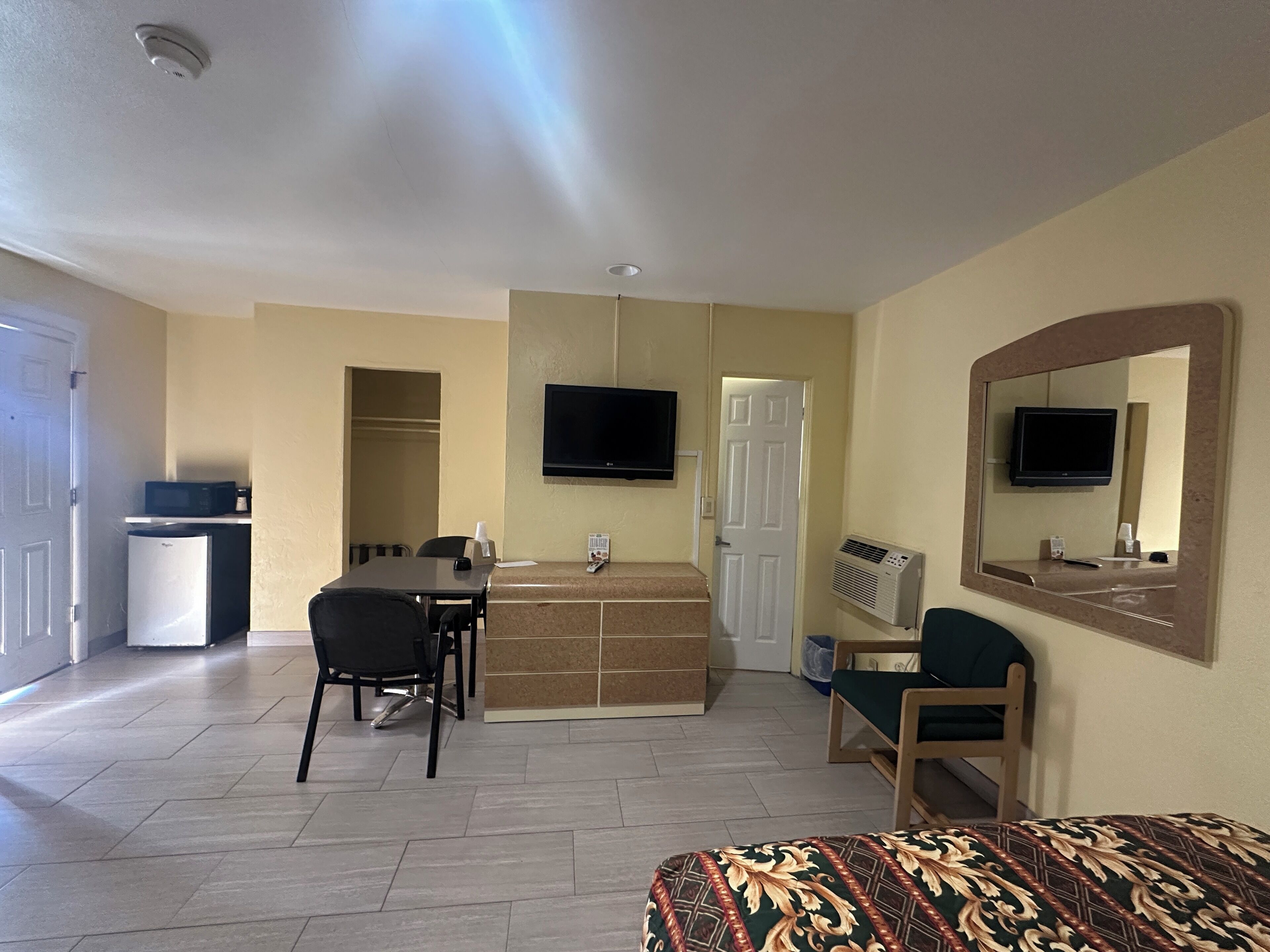 A hotel room with a bed, a desk, a chair, a television, a microwave, and a refrigerator.