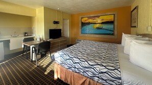 A hotel room with a bed, a desk, a chair, a television, and a painting of a sunset over water. - Super Inn (Daytona Beach)