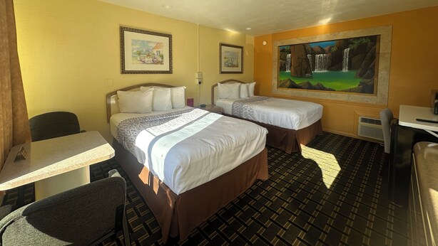 A hotel room with two beds, a desk, a chair, and a large painting on the wall. - Super Inn (Daytona Beach)