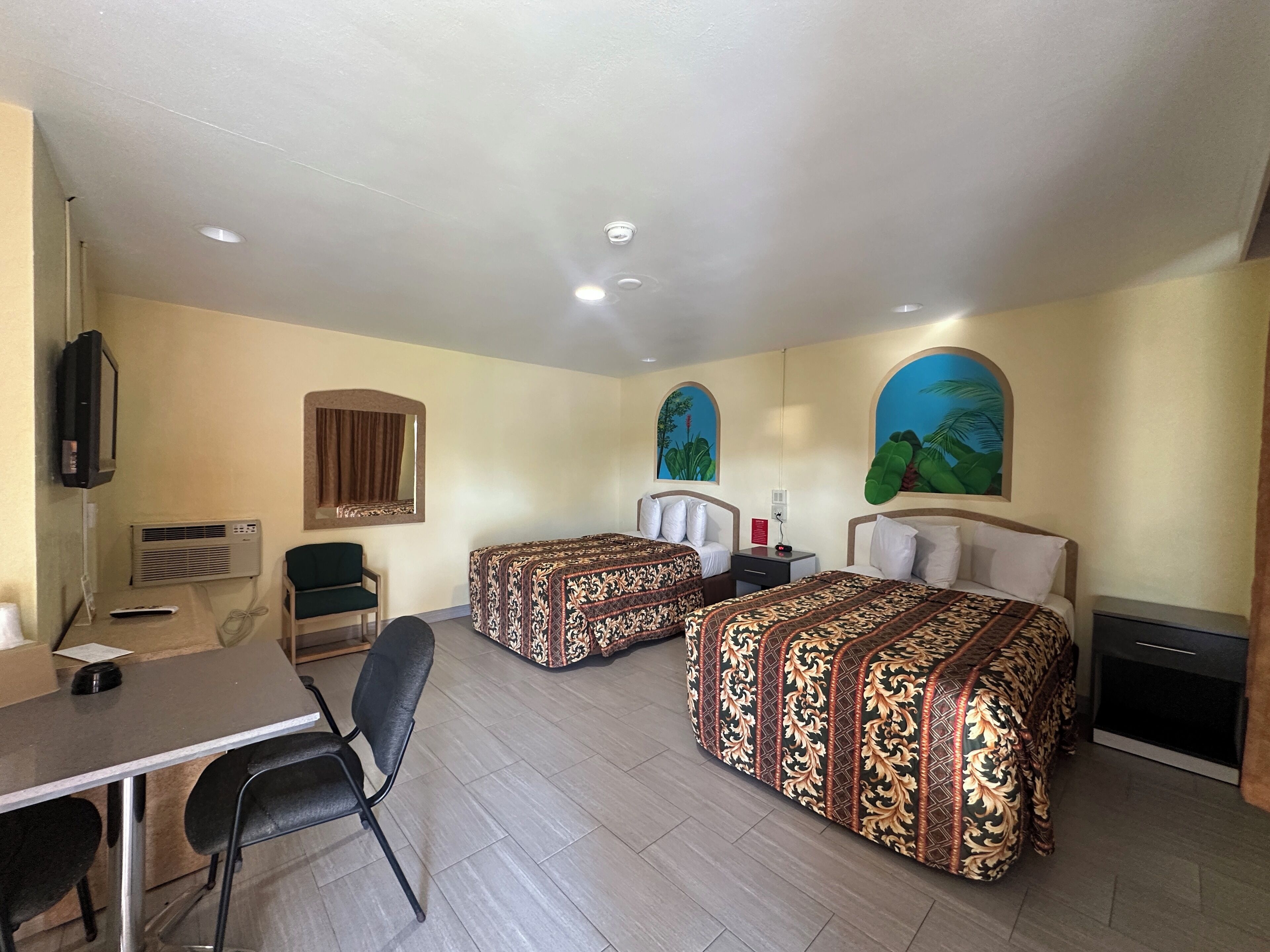 Une chambre d’hôtel avec deux lits, un bureau, une chaise, une télévision, un appareil de climatisation et un tableau au mur.