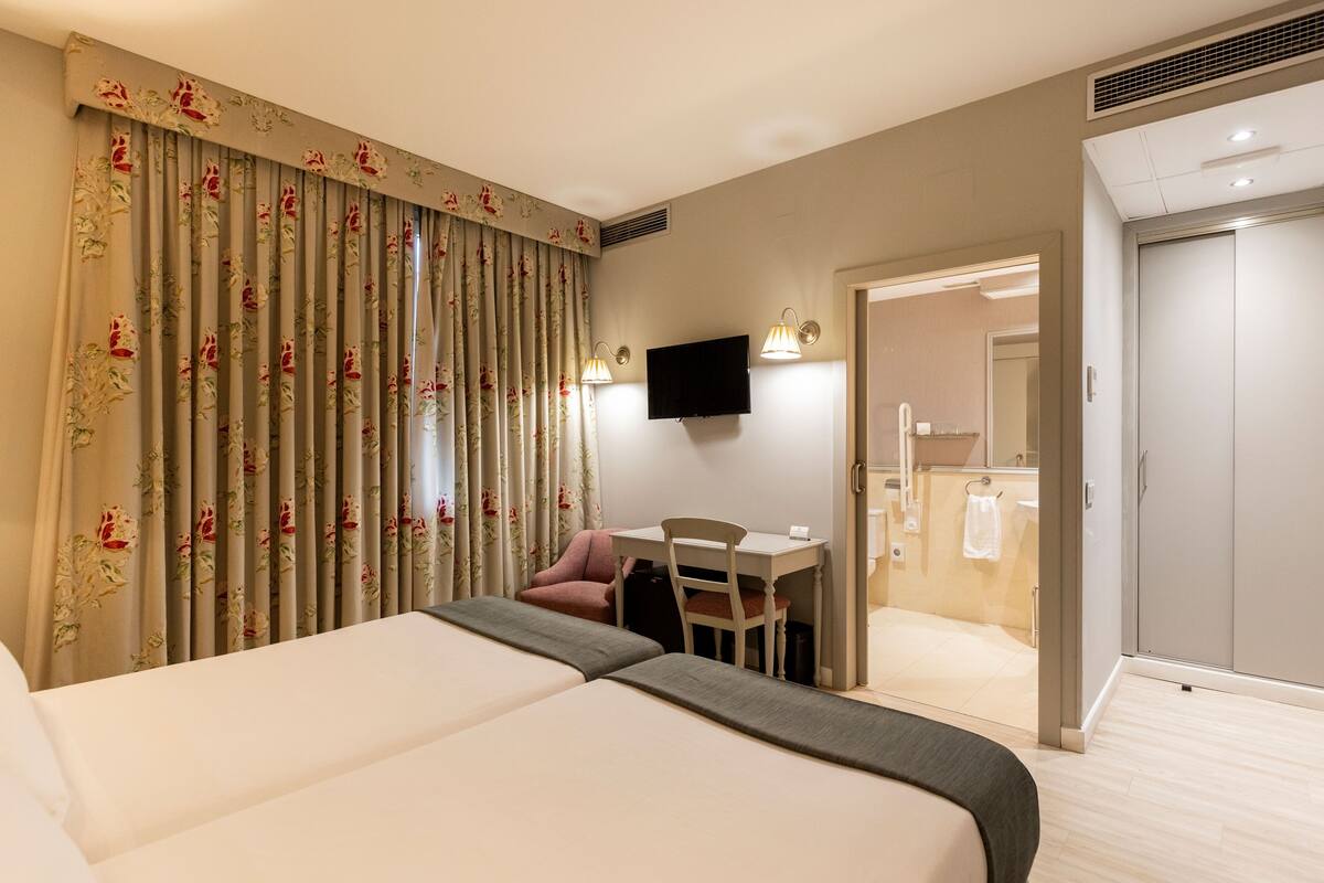 Een hotelkamer met twee bedden, een bureau met een stoel, een televisie en een badkamer zichtbaar door een geopende deur.