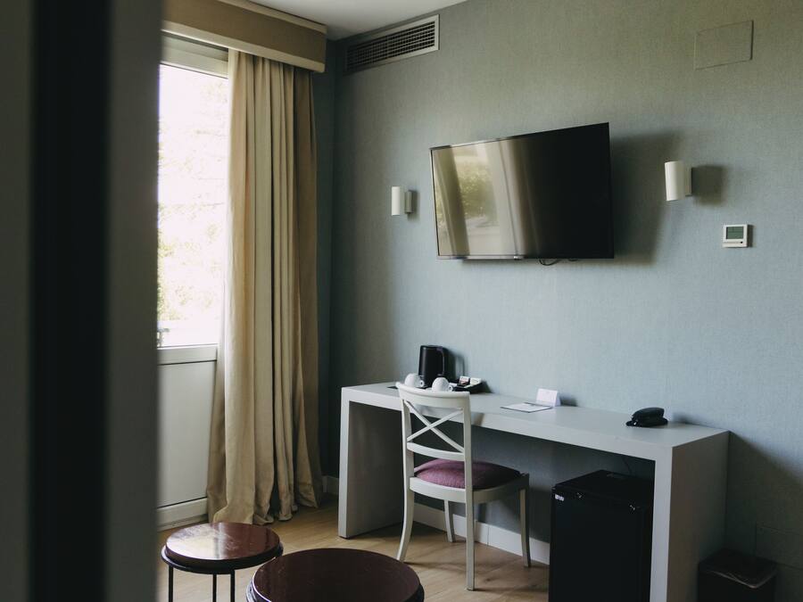 Ett hotellrum med ett skrivbord, en stol, en TV och en liten papperskorg.