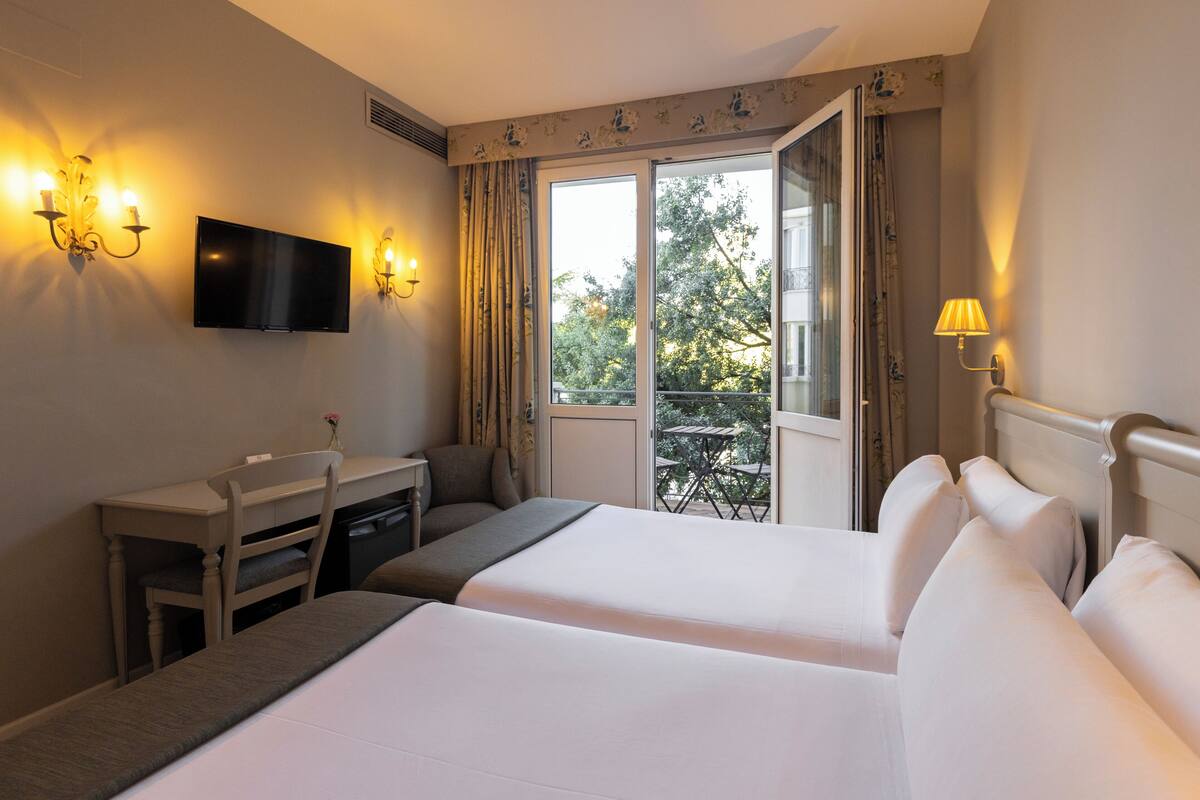 Een hotelkamer met een bed, een bureau, een stoel, een televisie en een balkon met een tafel en stoelen.