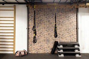 Un gimnasio con correas TRX suspendidas, una escalera de madera y un banco de pesas frente a una pared de ladrillo.