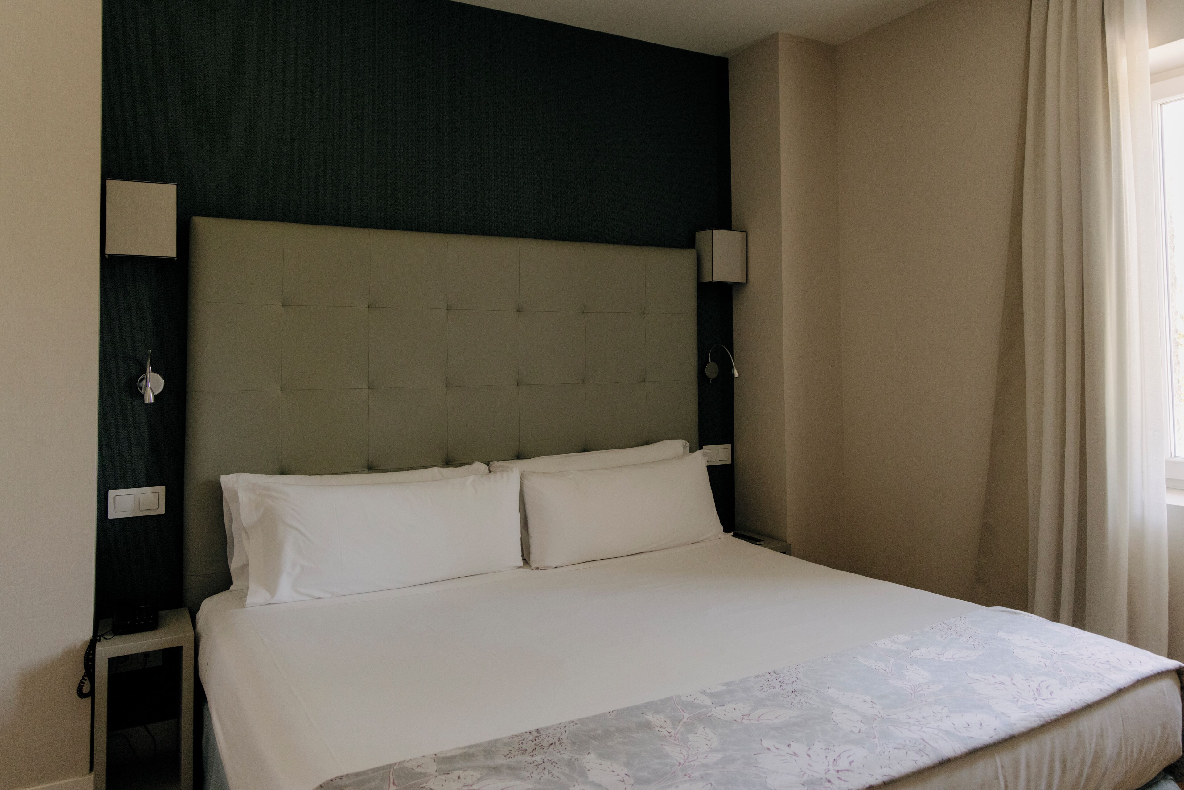 A hotel room with a large bed, a headboard, bedside lamps, and a nightstand.