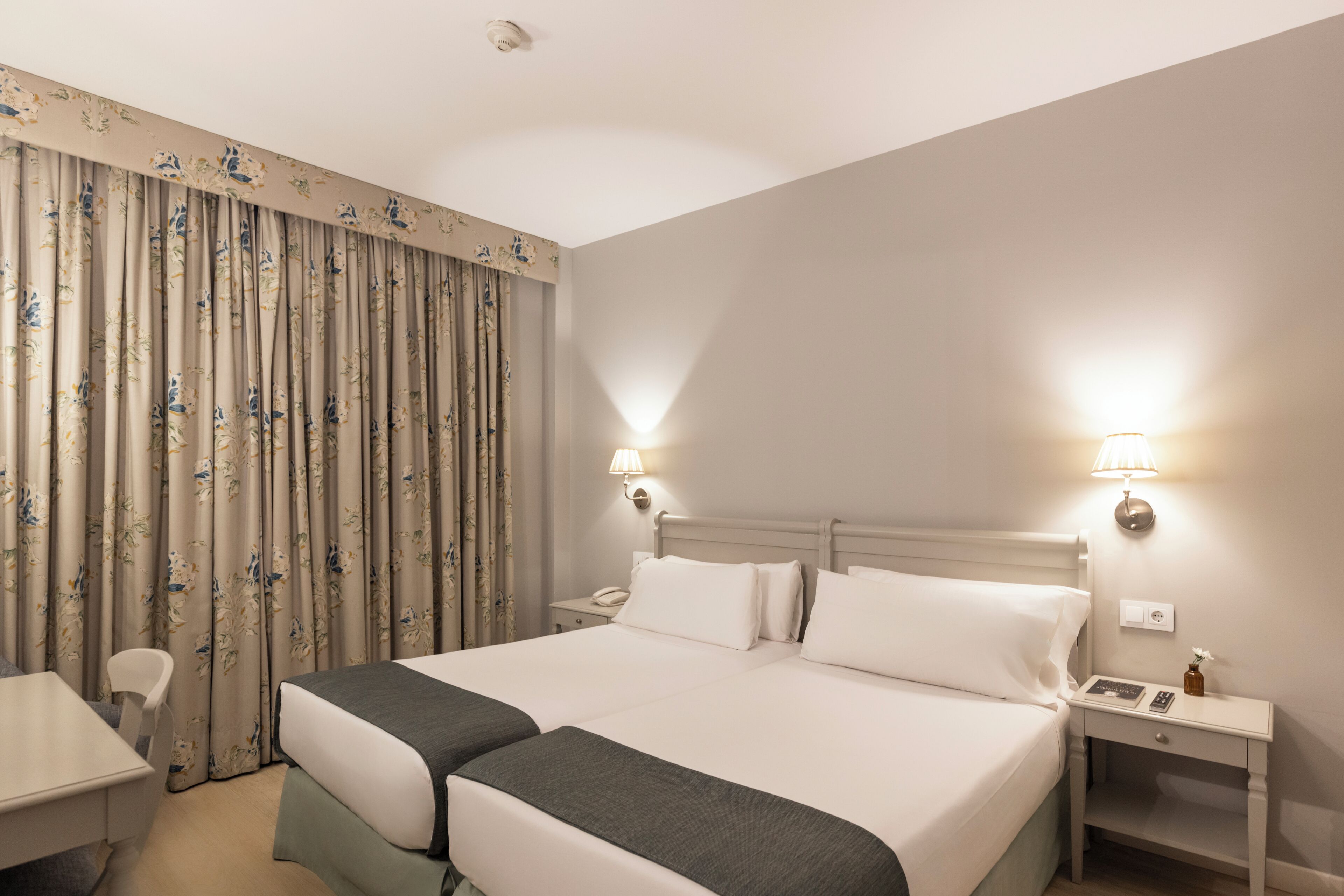 Una habitación de hotel con una cama doble, un escritorio, dos mesitas de noche, una lámpara y una silla.