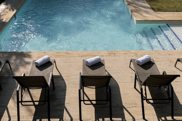 Zona de piscina con tres tumbonas, cada una con una toalla.