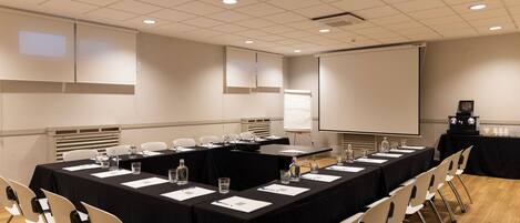 Un salón de conferencias con una larga mesa, sillas, una pantalla de proyector y una pizarra.
