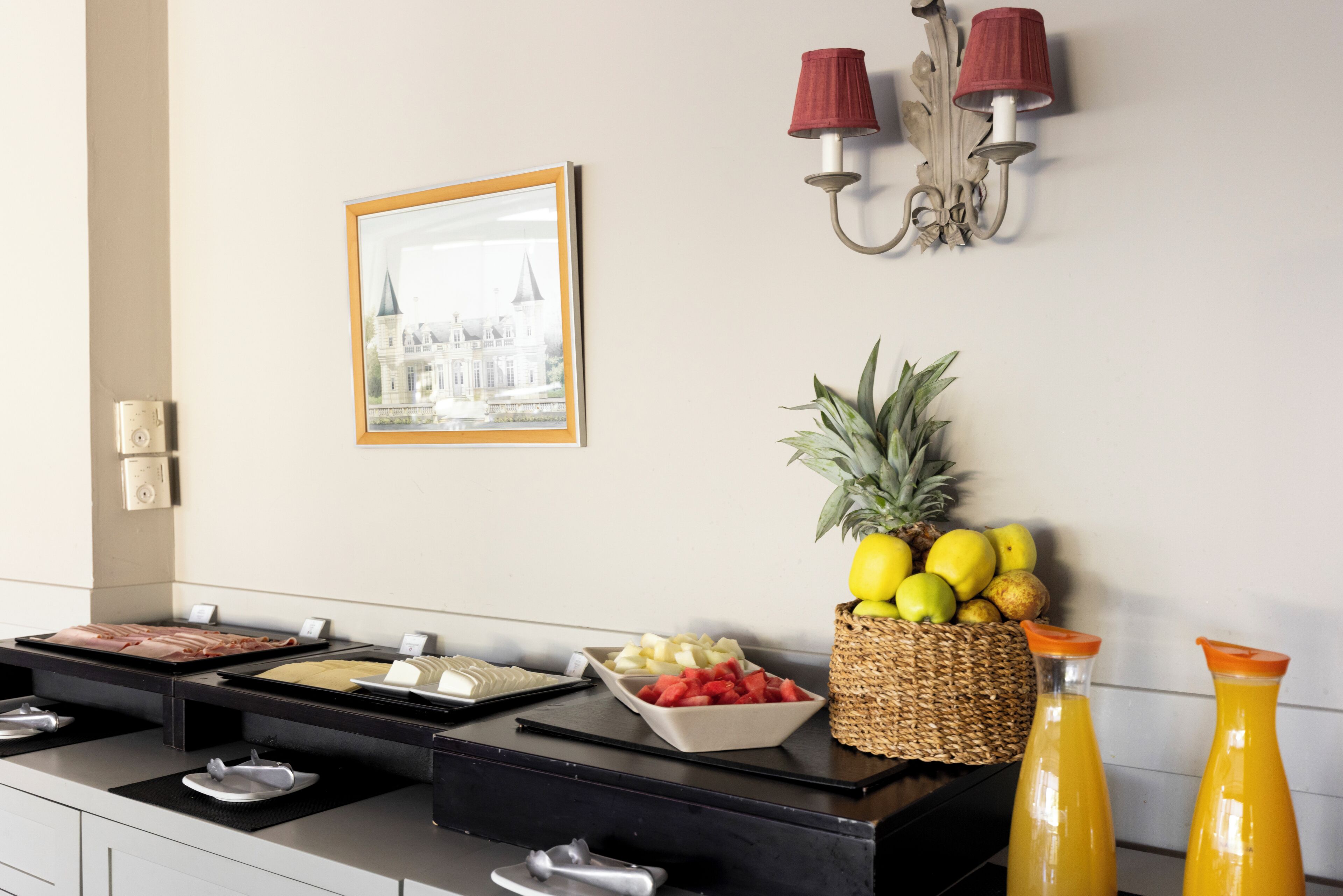 A buffet setup with various food items, a fruit basket, and two orange juice bottles.