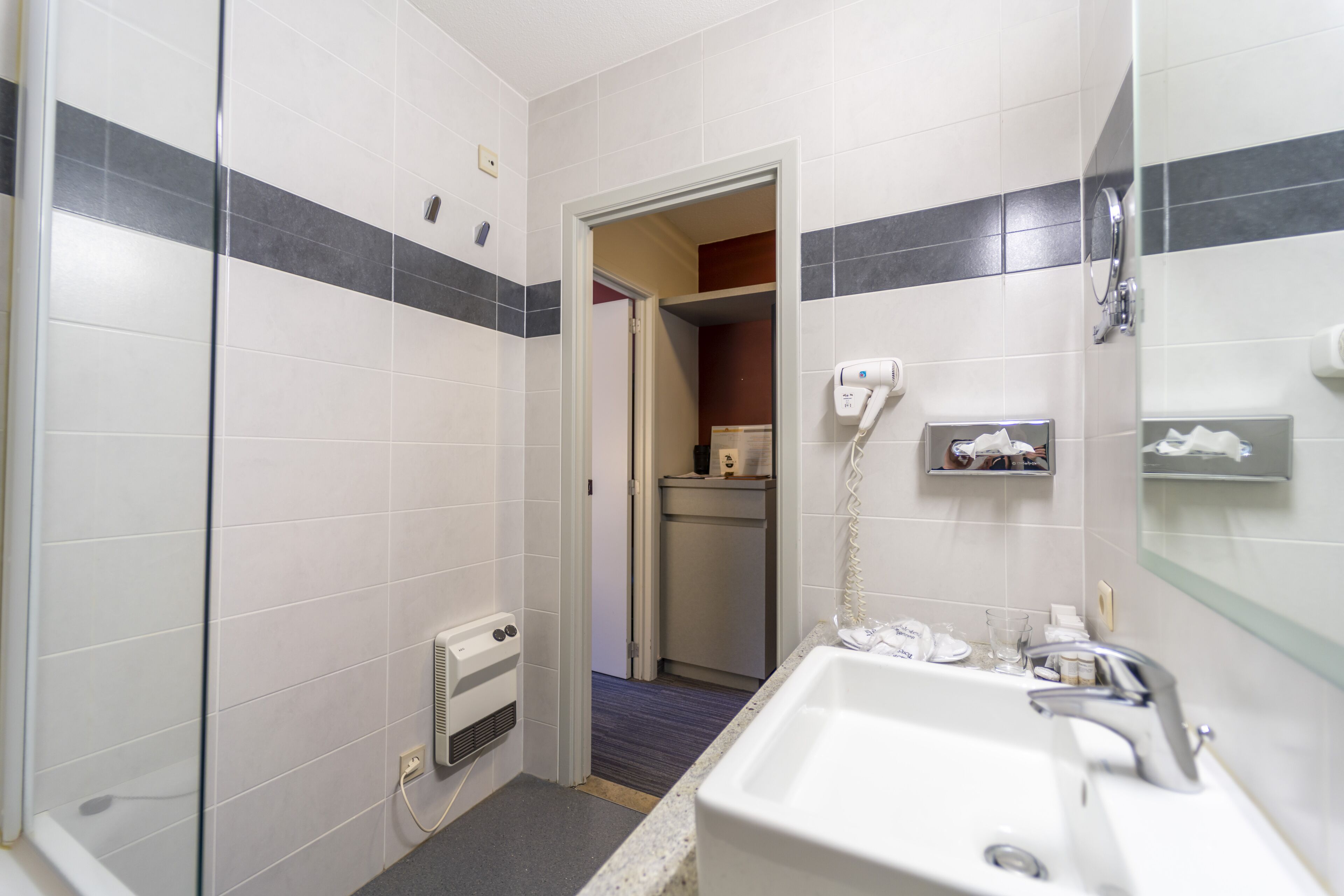 Un baño de hotel con ducha, lavamanos y espejo.