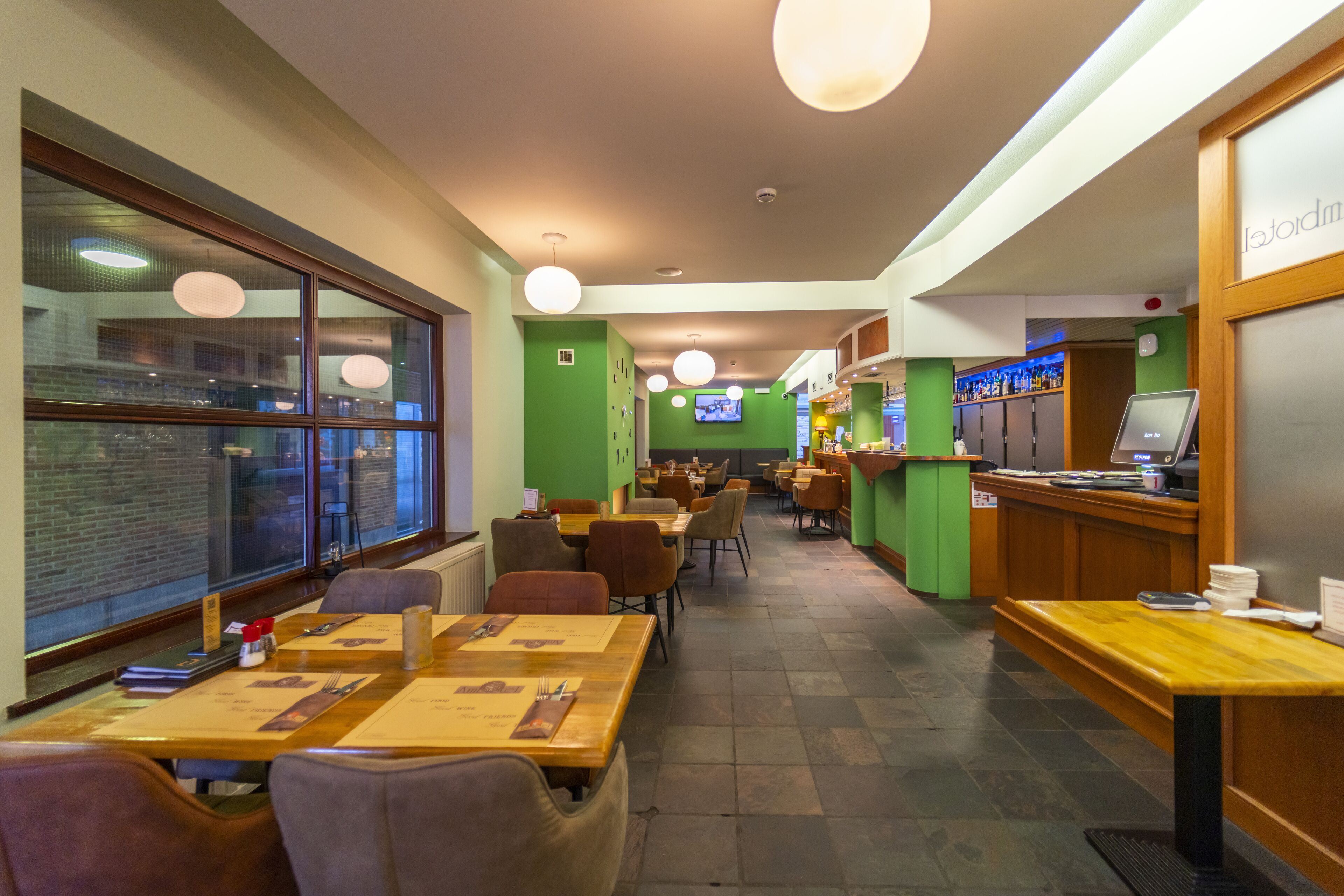 A restaurant with wooden tables and chairs, a bar area, and a television screen.
