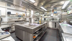 A commercial kitchen with stainless steel appliances, a central island, and various kitchen tools and supplies. - Ambiotel (Tongeren)