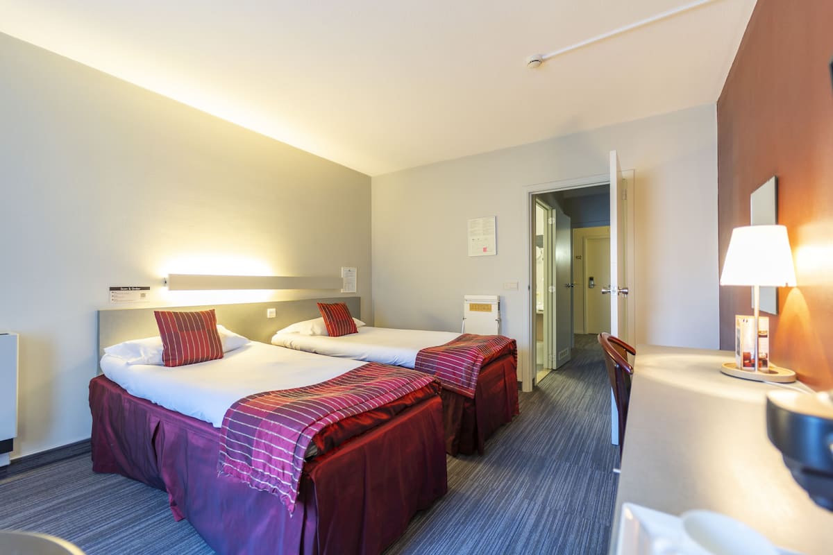 A hotel room with two beds, a desk, and a chair.
