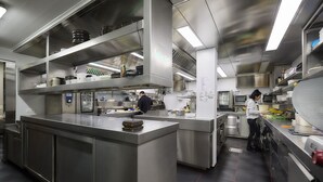 A commercial kitchen with stainless steel appliances, a central island, and two chefs working. - Ambiotel (Tongeren)