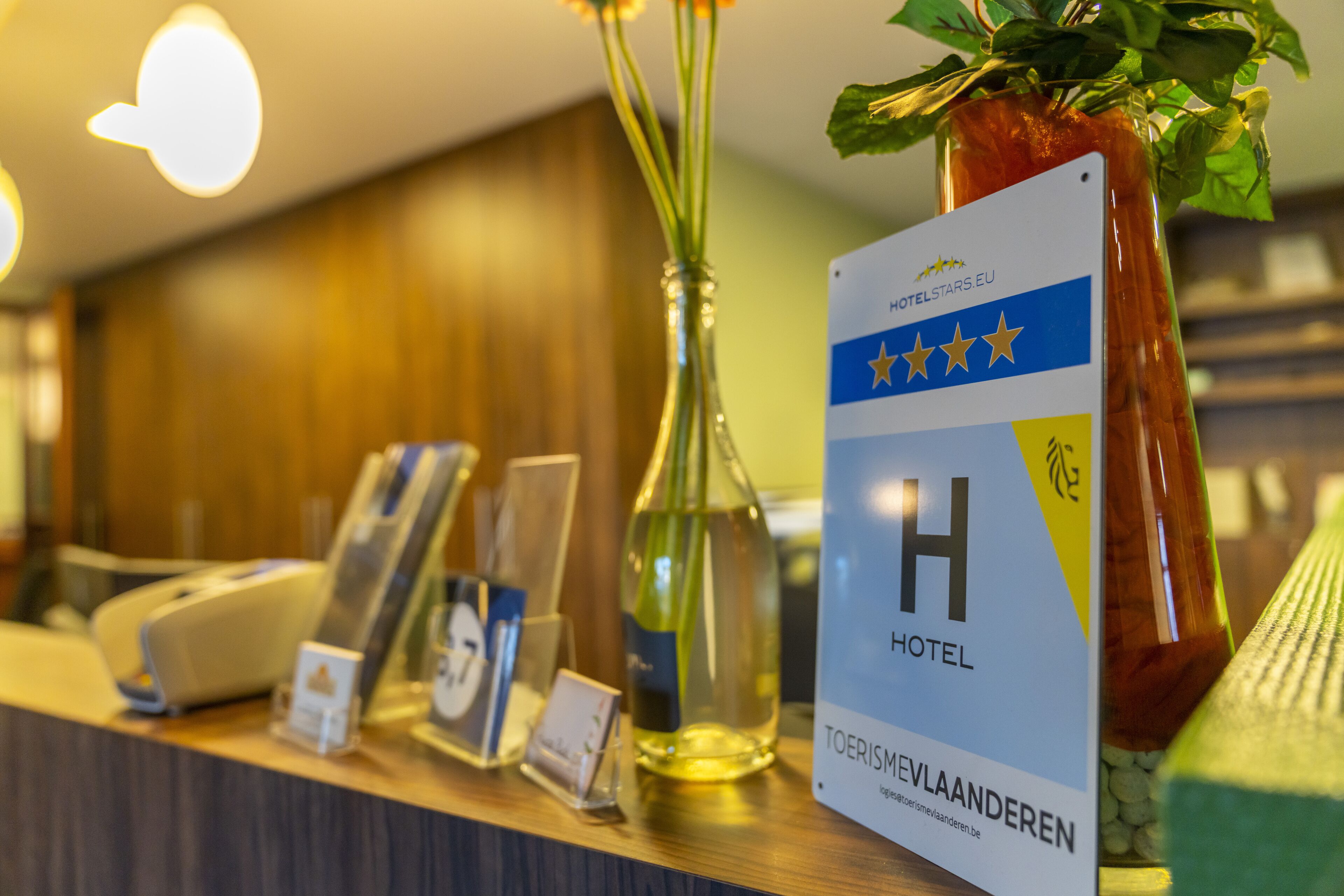 A hotel reception desk with a sign indicating it is a four-star hotel, a glass vase with a plant, and a bottle of wine.