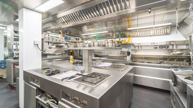 A commercial kitchen with stainless steel appliances, a large sink, and a ventilation hood. - Ambiotel (Tongeren)