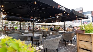 An outdoor seating area with wicker chairs and tables under black umbrellas with 'OMER' branding. - Ambiotel (Tongeren)