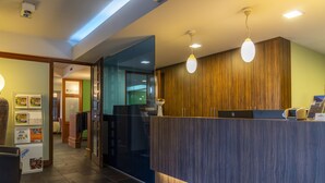 A reception area with a wooden reception desk, a glass partition, and a tiled floor. - Ambiotel (Tongeren)