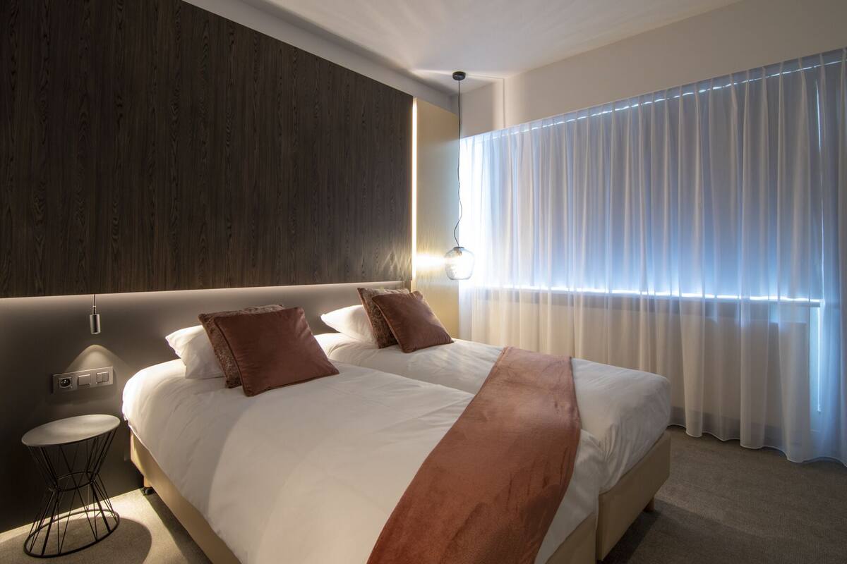 A modern hotel room with a large bed, a bedside table, and a wall-mounted light.