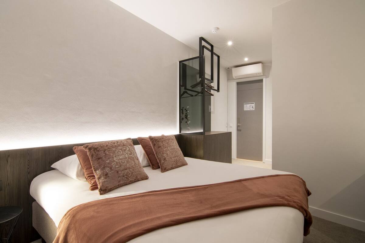 A modern hotel room with a large bed, a bedside table, a mirror, and a wardrobe.