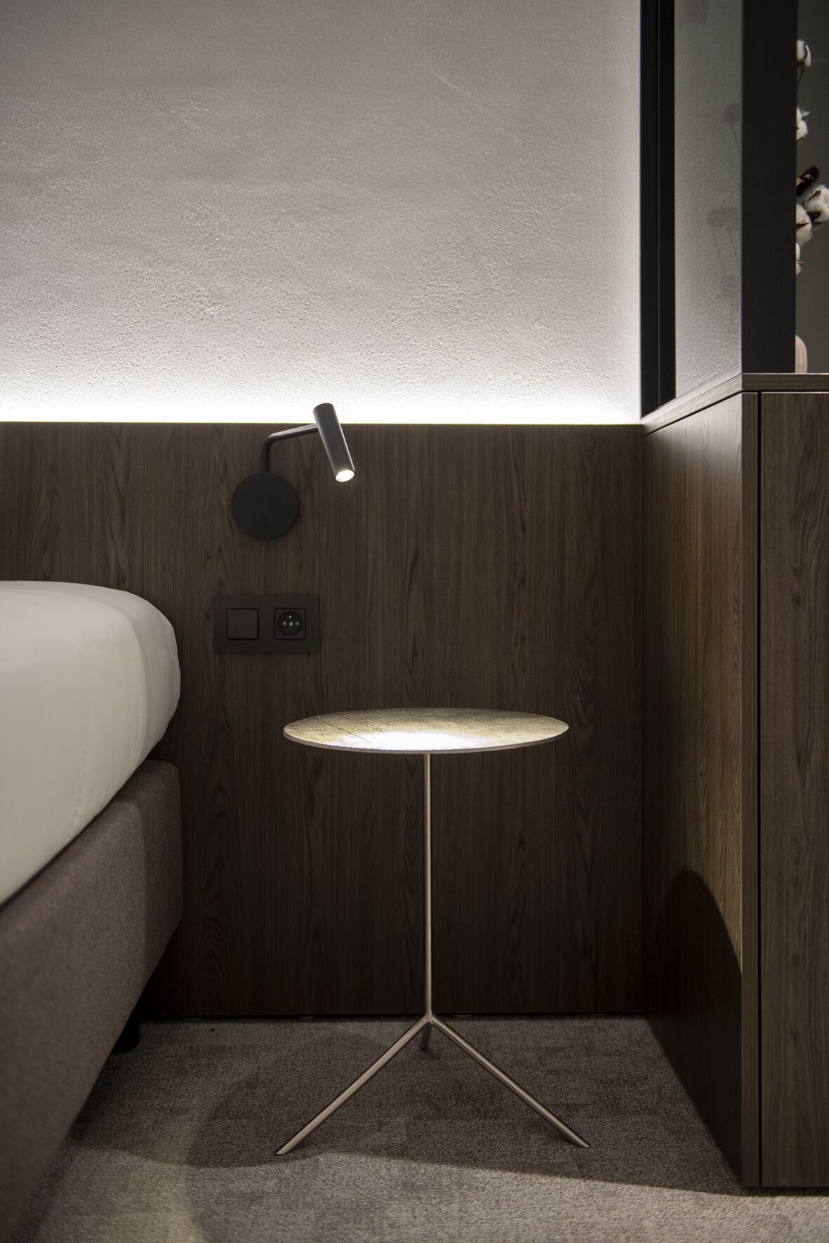 A modern bedroom with a bed, bedside table, and a wall-mounted lamp.