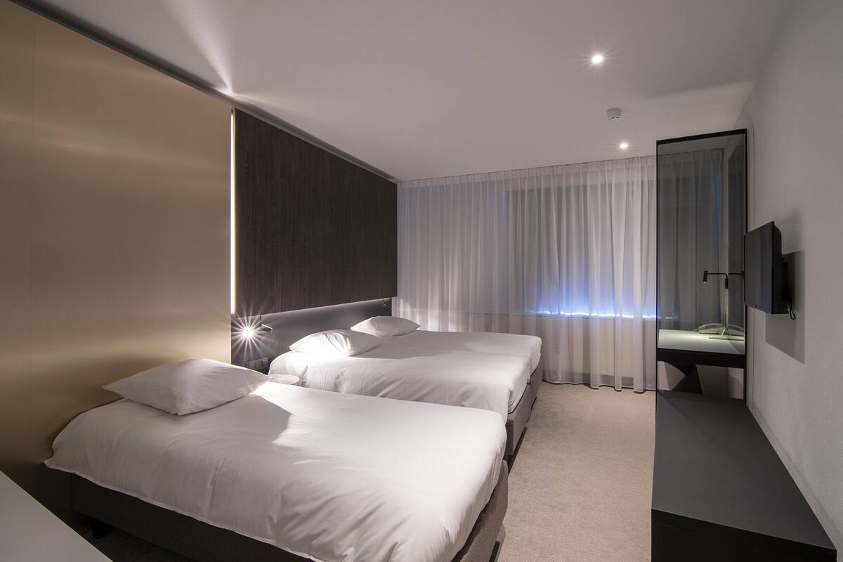 A modern hotel room with two beds, a large mirror, and a TV.