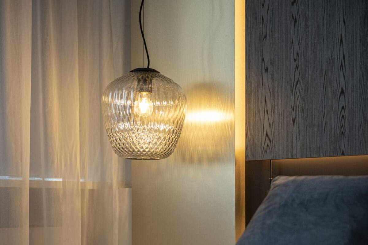 A neatly made bed with a grey pillow, a textured hanging light fixture, and a wooden headboard.