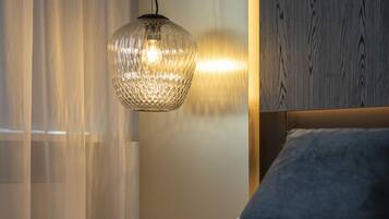 A neatly made bed with a grey pillow, a textured hanging light fixture, and a wooden headboard.
