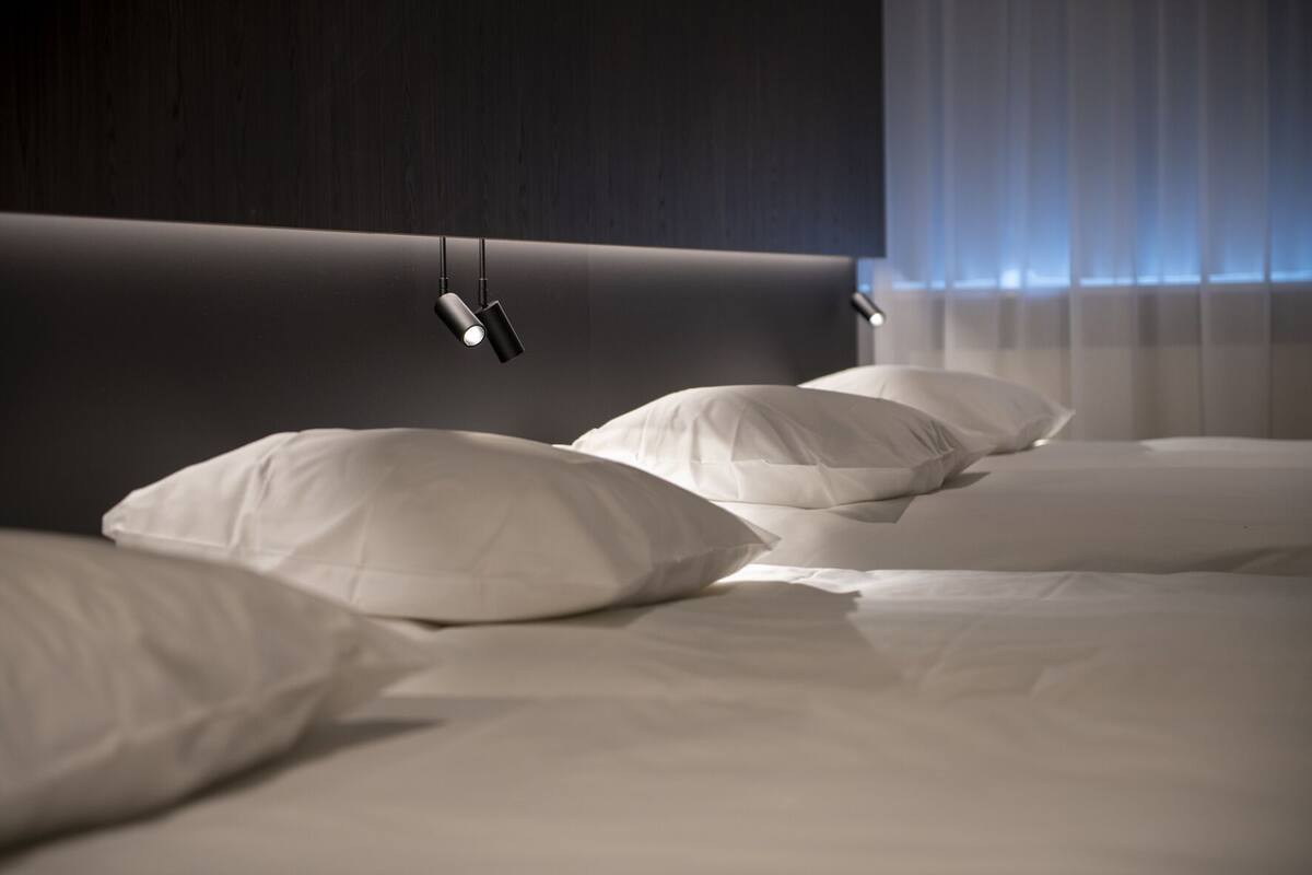 A neatly made bed with white bedding and pillows, a dark headboard, and a modern pendant light fixture.
