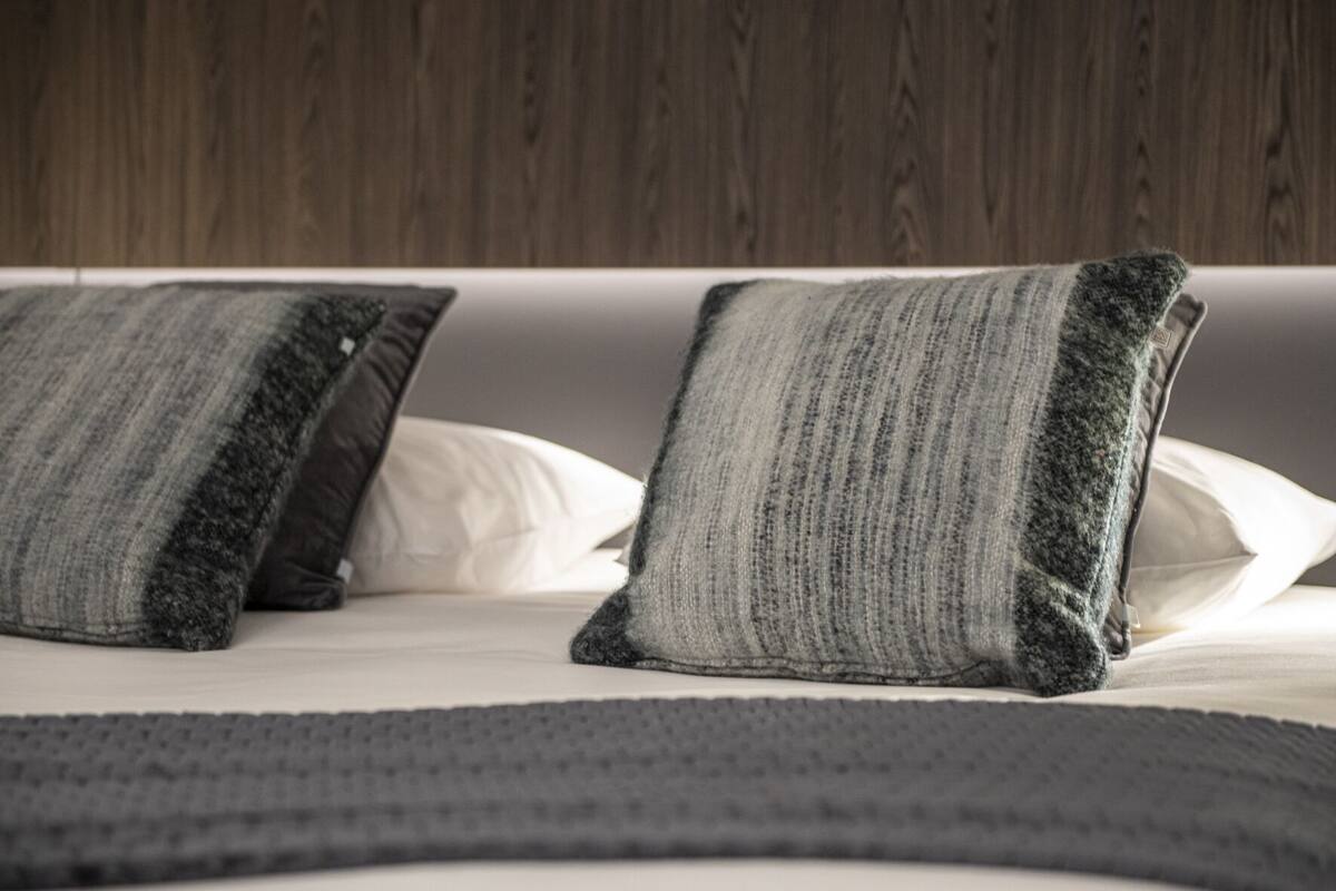 A bed with striped pillows and a grey blanket.