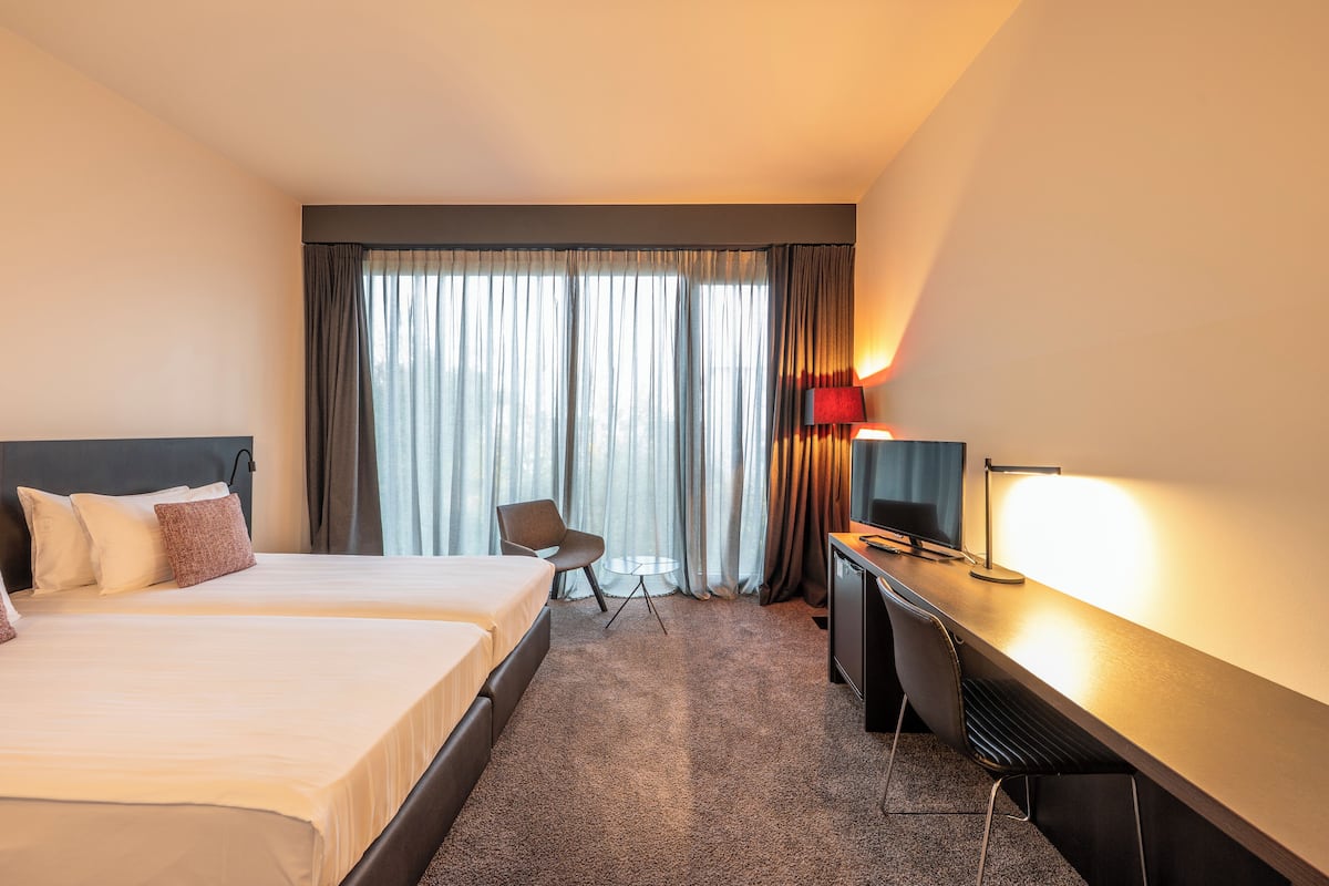 A hotel room with two beds, a desk with a TV, and a chair.