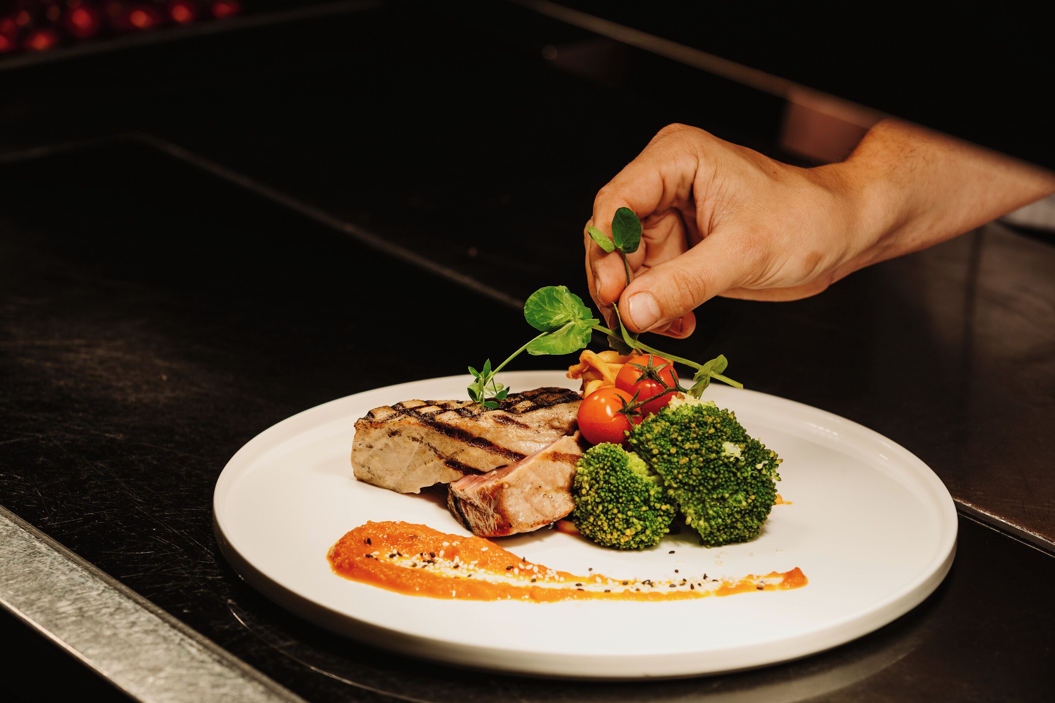 A plate with grilled meat, broccoli, and cherry tomatoes, garnished with a sprig of herb.