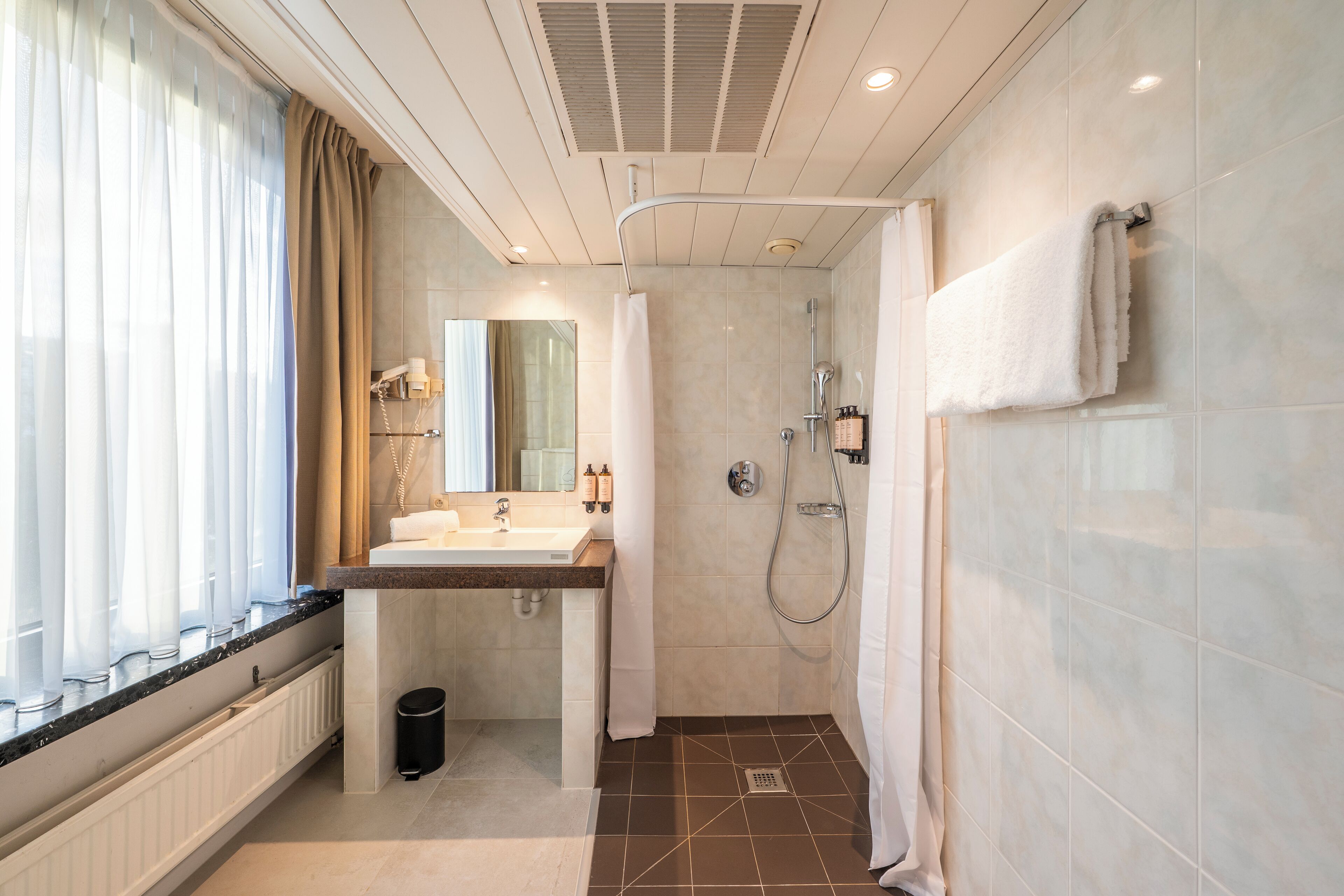 A modern bathroom with a sink, mirror, shower, and towel rack.