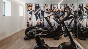 Une salle de sport équipée de nombreux appareils d’exercice, dotée d’un grand mur de miroirs et d’un plancher en bois.