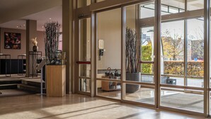 Un hall d’hôtel moderne doté d’une grande porte vitrée, d’un comptoir d’accueil et d’un escalier menant à l’étage supérieur.