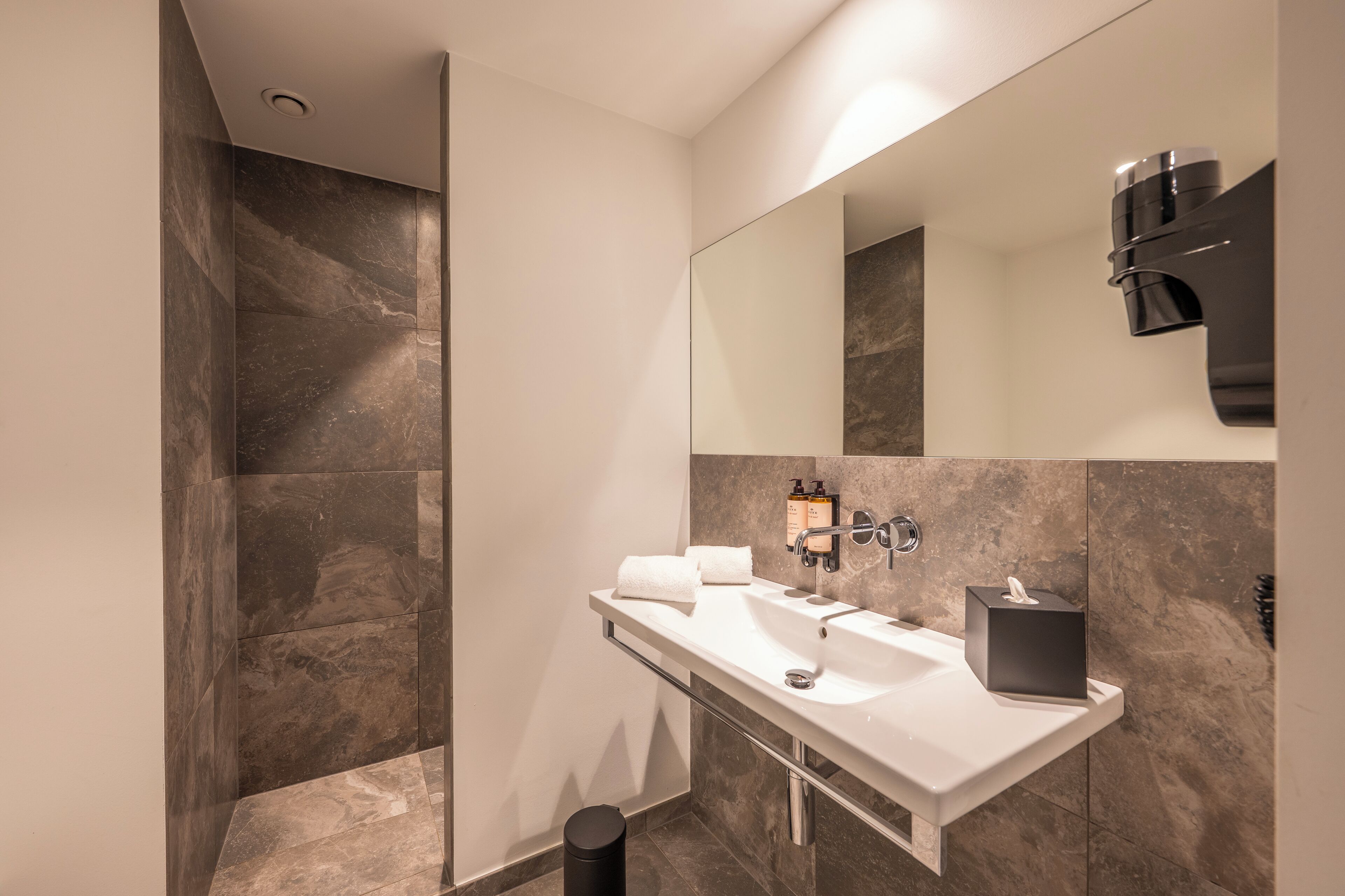 Un baño moderno con ducha a ras de suelo, un espejo grande y un mueble de tocador con lavabo y toallero.