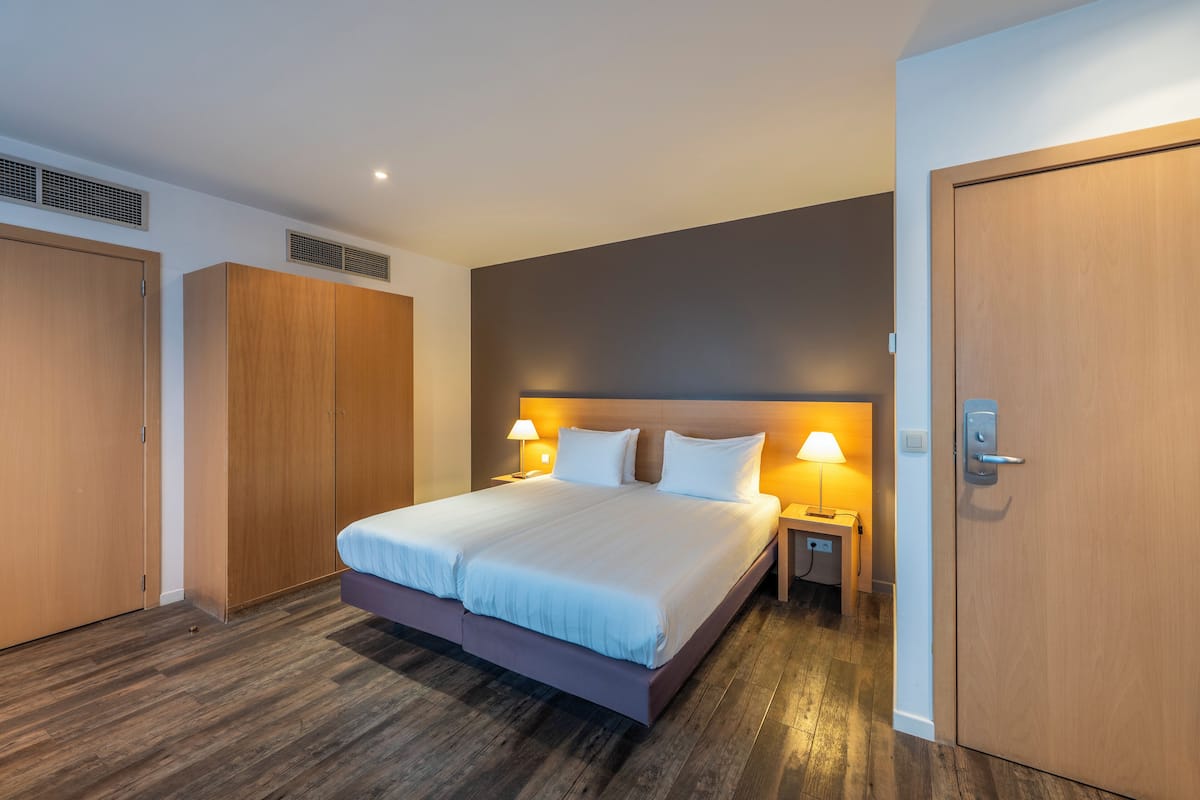 A modern hotel room with a large bed, two bedside tables, and a wardrobe.