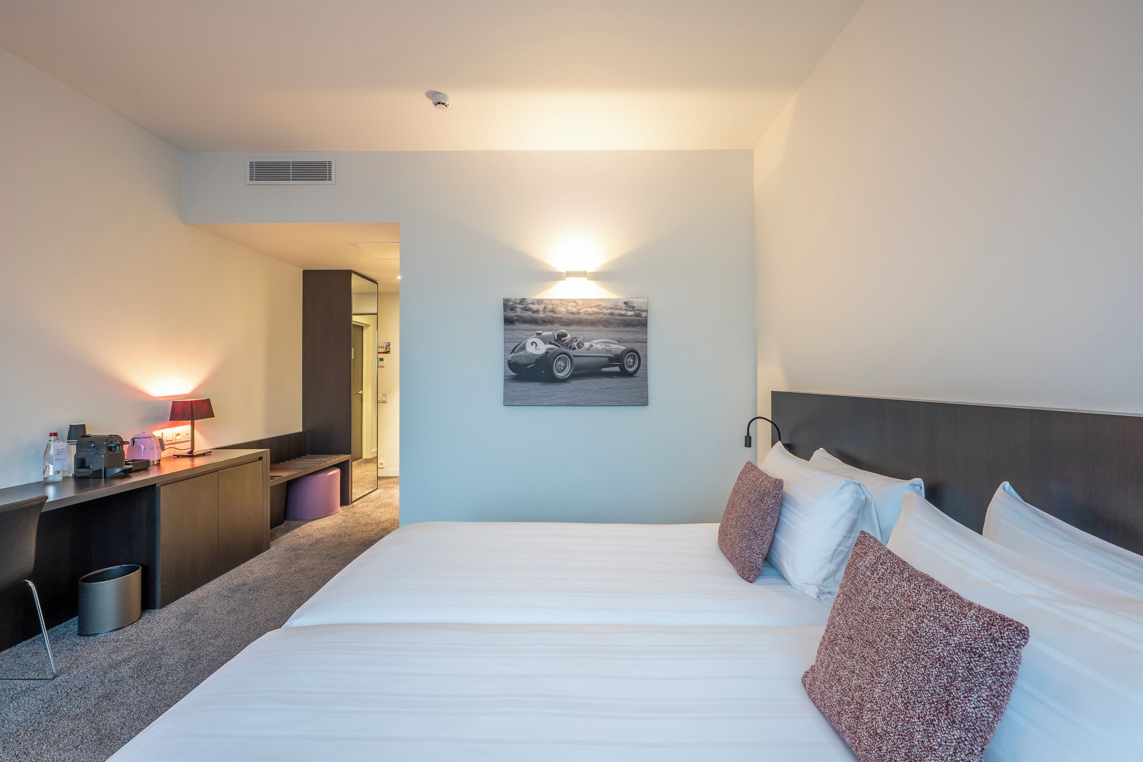 A hotel room with a bed, bedside table, lamp, and a wall-mounted picture.