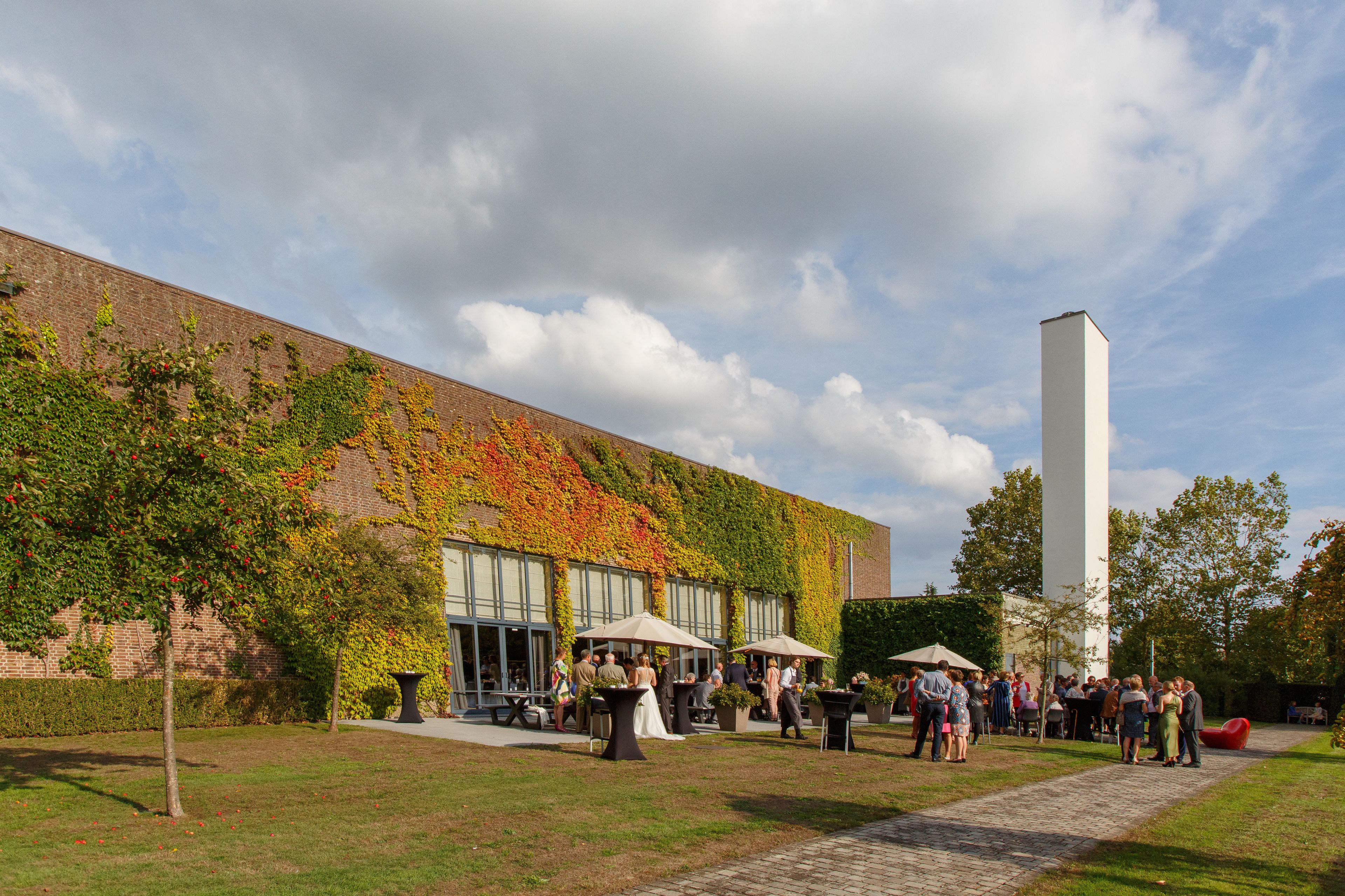 An outdoor gathering area with a brick building, a tall white column, and a paved walkway.